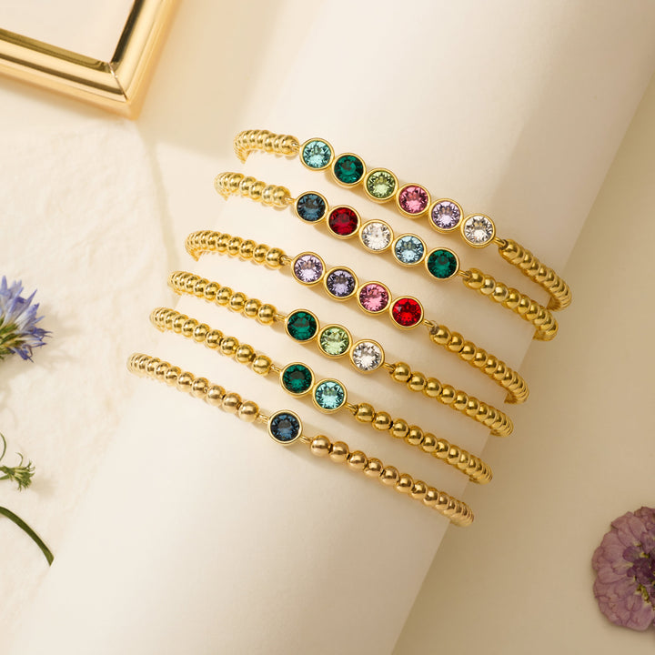 Set of birthstone bead bracelets, each with bezel-set round birthstones in varying colors and counts, stacked on a display.