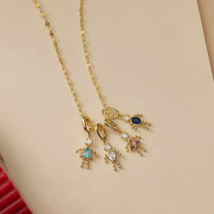 Necklace with three dangling child figure charms, each set with a different colored birthstone, arranged on a display in a close-up shot.