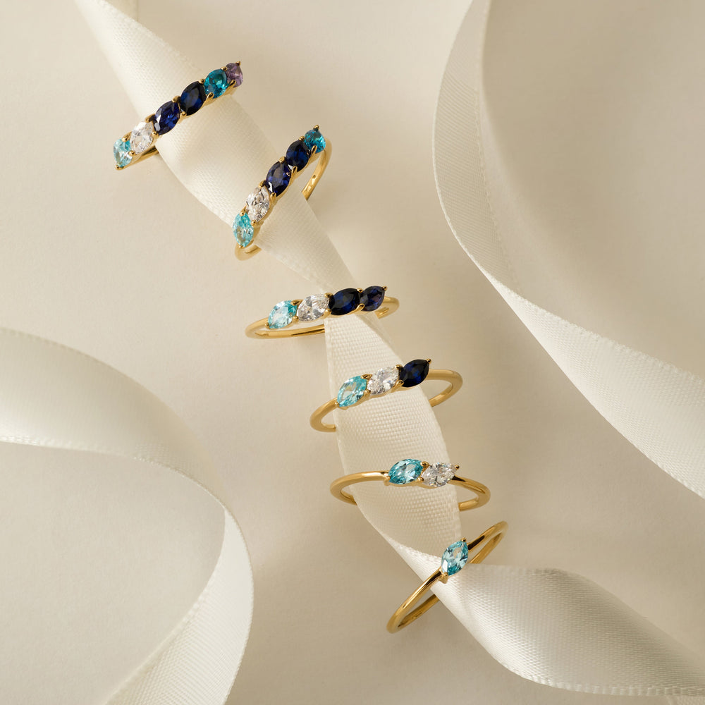 Collection of Custom Petal Marquise Birthstone Rings arranged on ribbon, each band set with marquise-cut stones in varying birthstone color combinations.