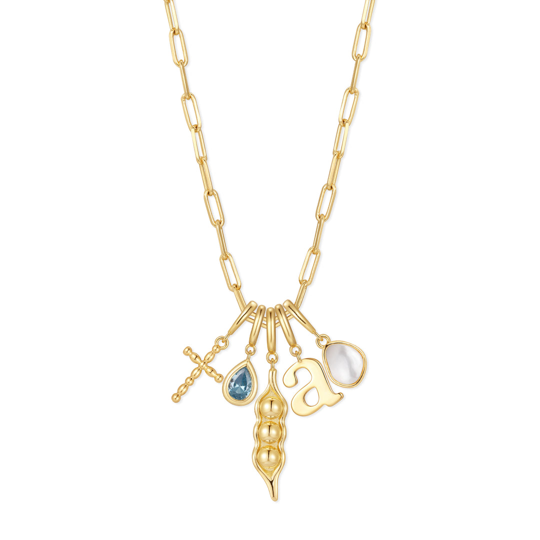Gold-tone charm necklace with five charms: a cross, pear-cut blue stone, pea pod, script initial, and pear-shaped mother-of-pearl pendant, on a chain.