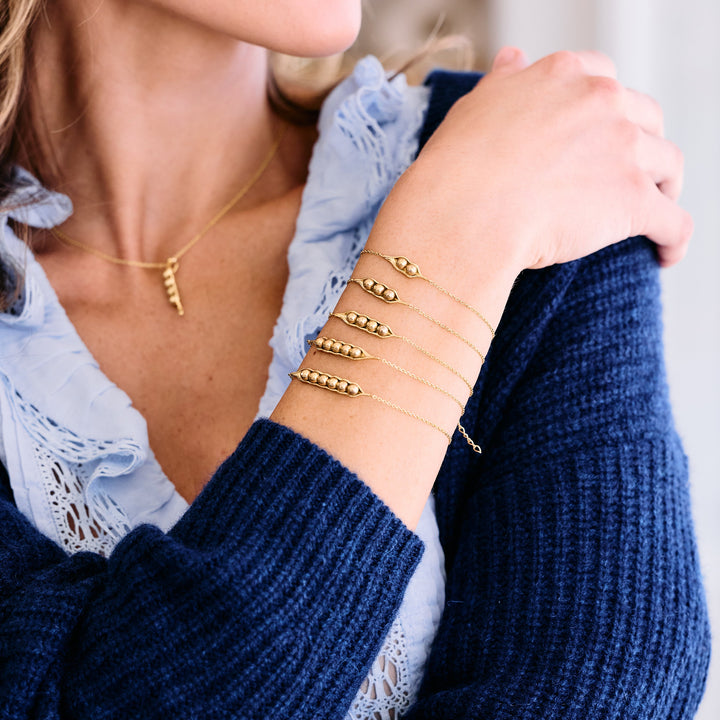 Stack of five Peas in a Pod bracelets with varying pea counts in the pod charm, worn by a model.