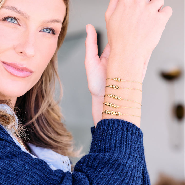 Set of five Peas in a Pod bracelets with varying numbers of pea-shaped beads in pod charms on delicate chains, worn by a model.