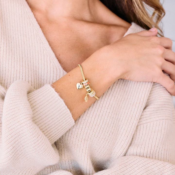 Charm bracelet worn by a model, styled with a heart charm, pink enamel flower bead, pavé ring bead, and a small oval initial charm.