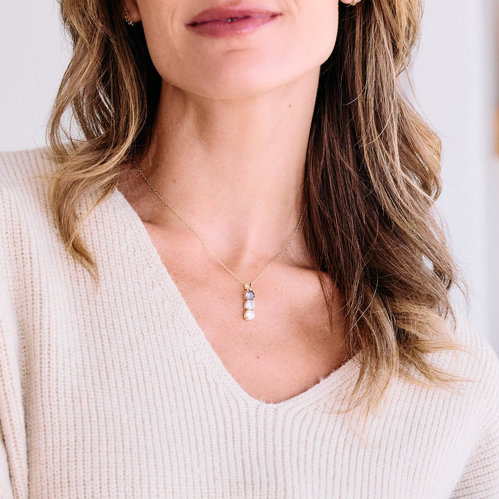 Three-stone birthstone pendant necklace with round prong-set stones in a vertical drop, worn by a model.