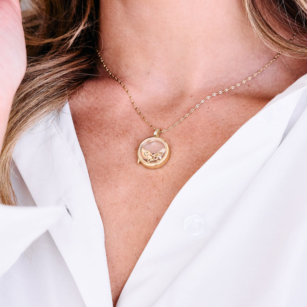gold chain with gold round glass locket with rainbow charm, cherry charm on women's neck wearing white shirt.