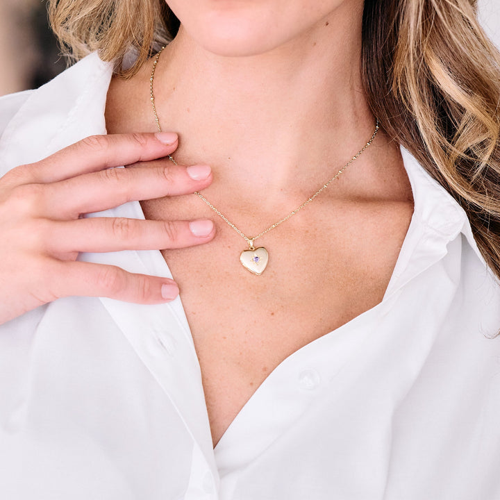 Heart locket necklace with a star-set birthstone center worn by a model, suspended on a delicate chain.