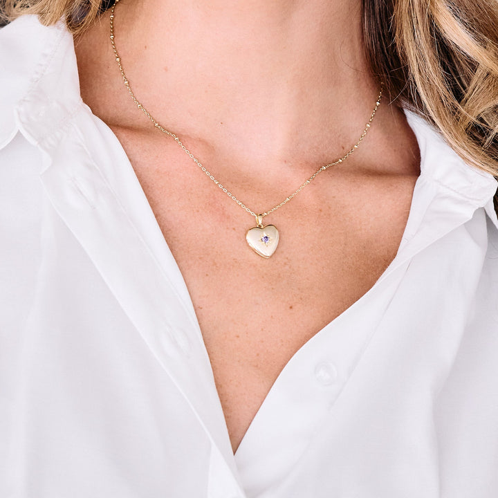 Heart locket necklace with a birthstone set in a star engraving, worn by a model.