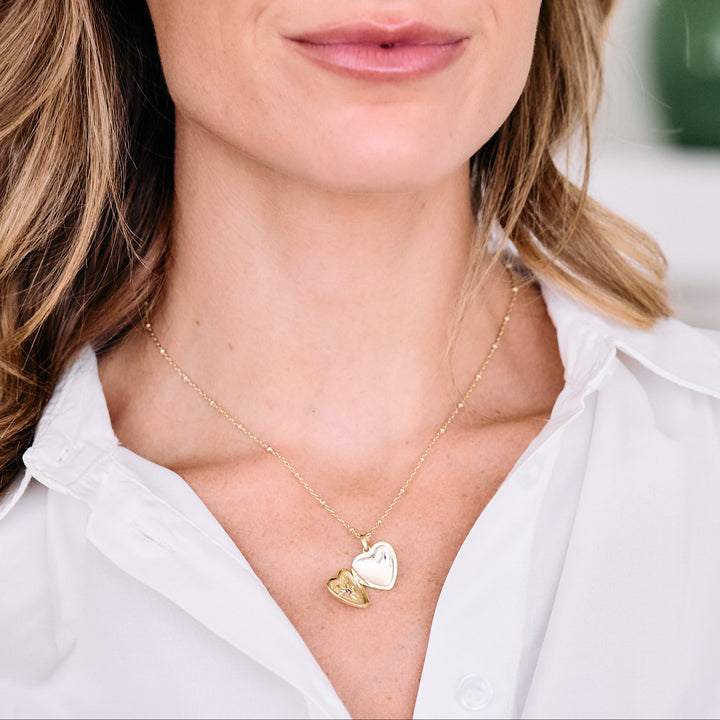 Heart locket necklace with a star-set birthstone worn by a model, open to reveal the interior and engraved star detail on the lower half.