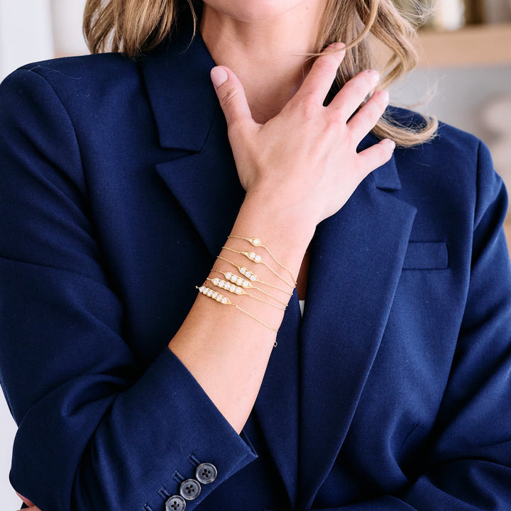 Set of five evil-eye chain bracelets with varying numbers of bezel-set moissanite stones, worn by a model.
