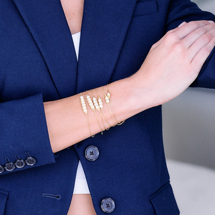 Three chain bracelets with varying numbers of pearl-set pod-shaped pendants, worn by a model, stacked at the wrist.