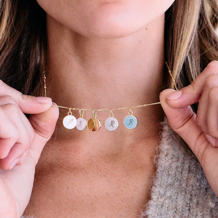 Multi-initial charm necklace with five round script-engraved discs in mixed colors worn as a choker by a model.