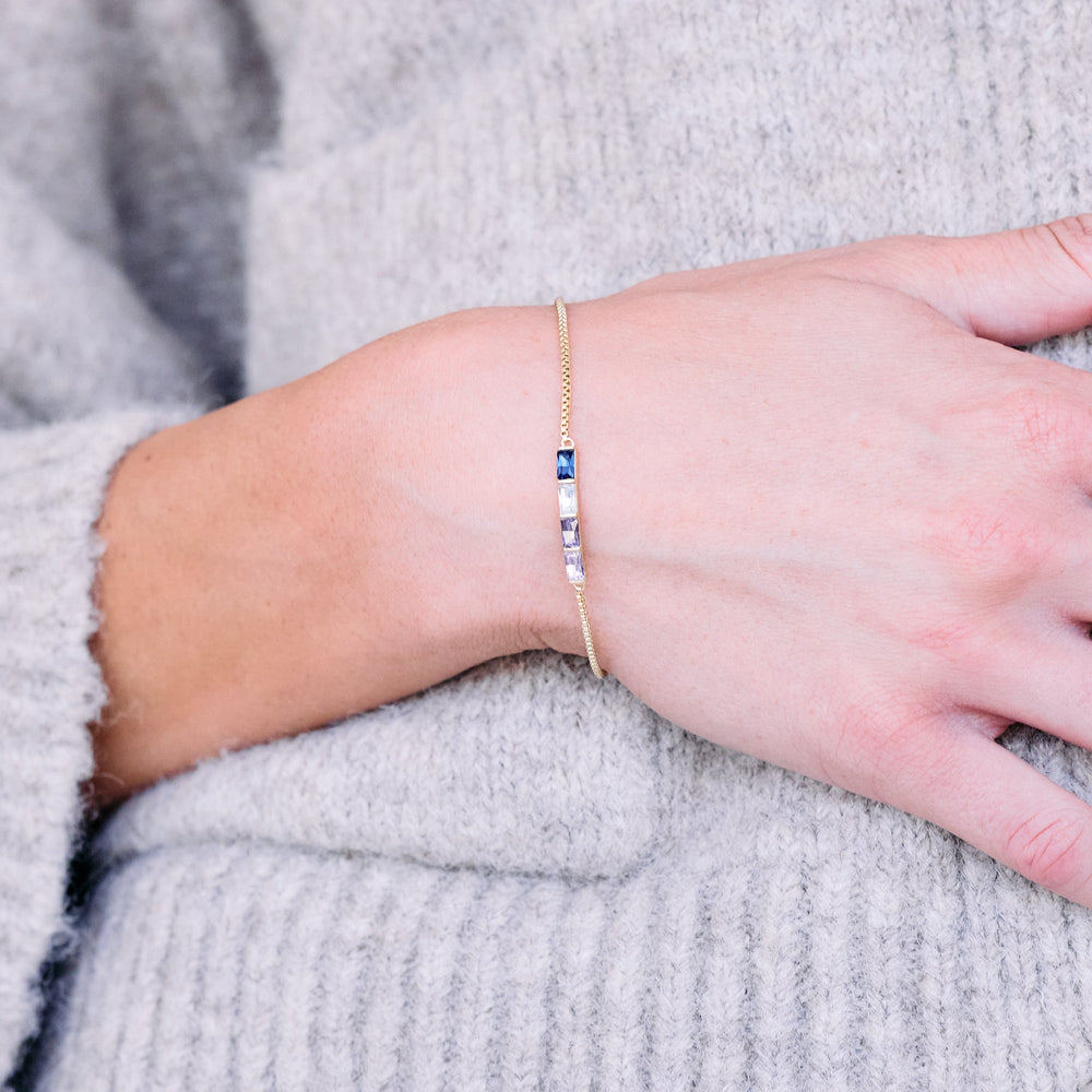 Birthstone bracelet with a row of rectangular baguette-cut birthstones on a delicate chain, worn by a model.