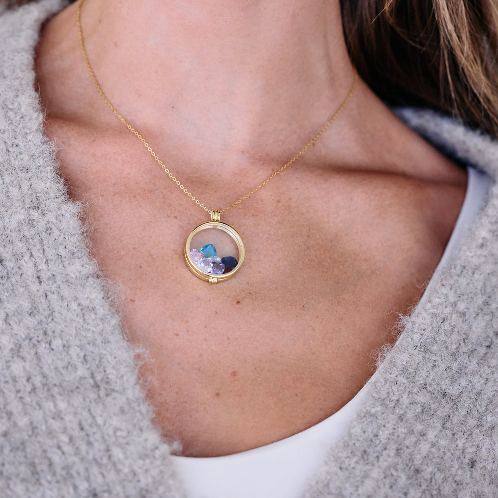 Round glass floating locket necklace with loose birthstone gems inside, worn by a model, on a delicate chain.