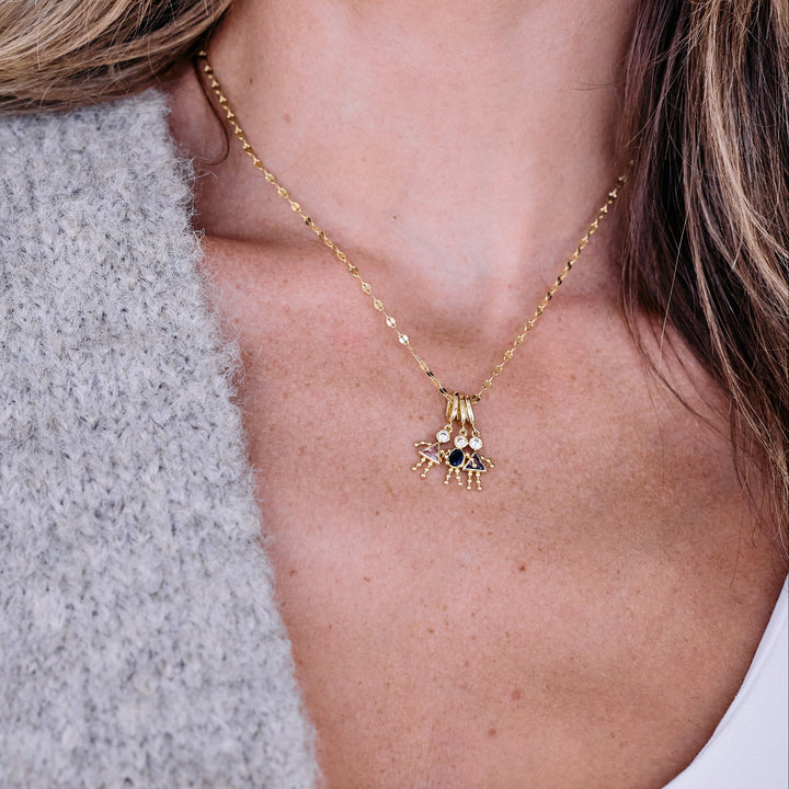 Child charm necklace with three birthstone figure pendants on a chain, worn by a model, each charm set with a round stone and triangular or oval birthstone body.