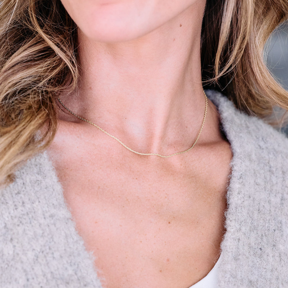 Delicate chain necklace worn by a model, sitting close to the collarbone with a fine-link design that catches the light.