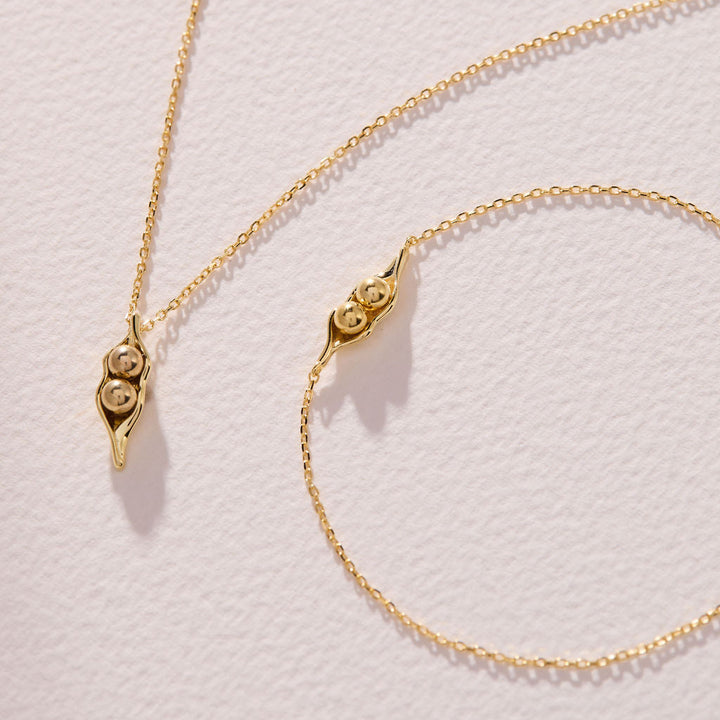 Two pea pod necklaces on a chain, each with a different number of round peas nestled in the pod pendant.