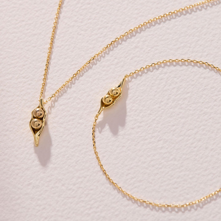Two Peas in a Pod bracelets with pea-pod charms on delicate chains, one with two peas and one with three peas.