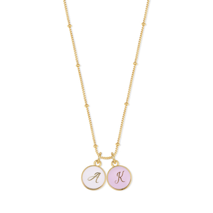 Initial charm necklace with two round script-engraved discs in white and pink enamel hanging from a chain with small ball accents.