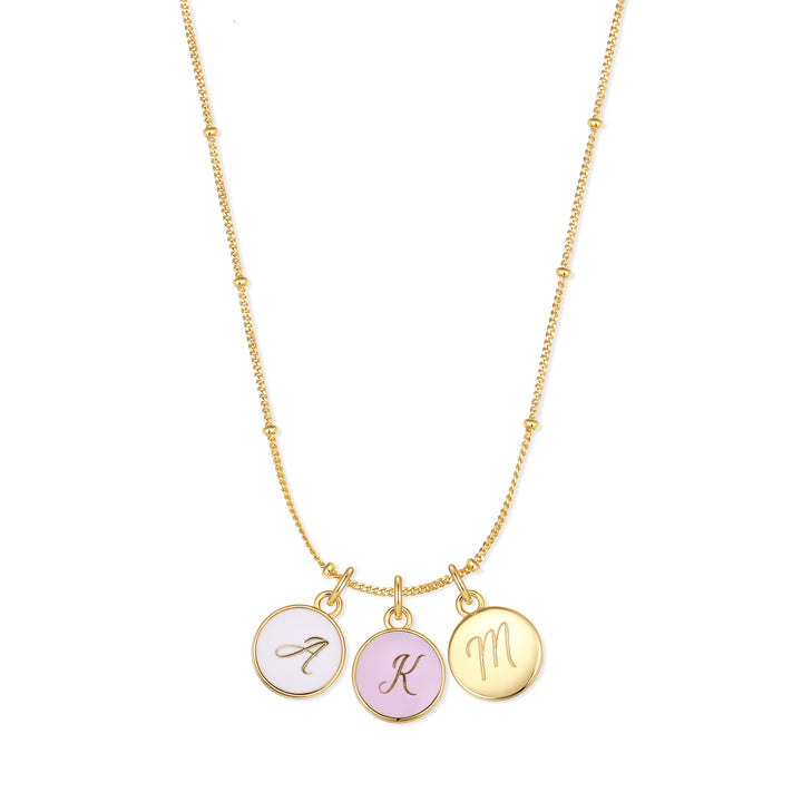 Initial charm necklace with three round script-engraved discs — one white enamel, one lavender enamel, one polished — on a chain.